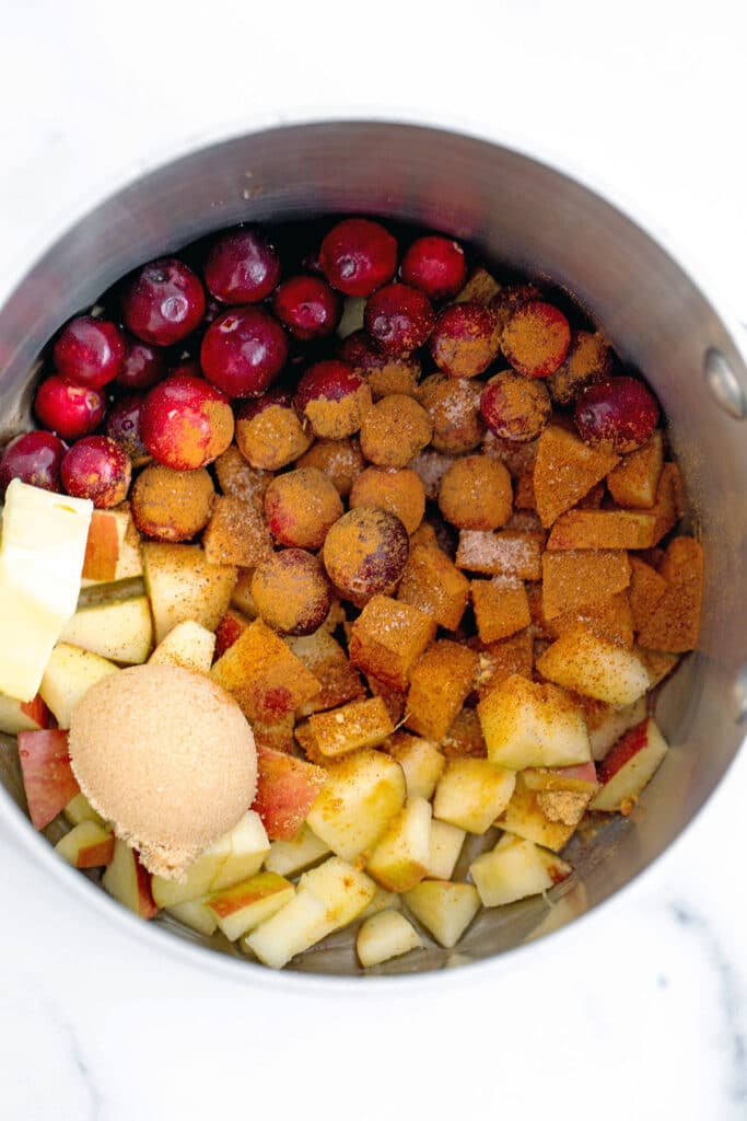 Overhead view of cranberries, apples, brown sugar, and butter in saucepan
