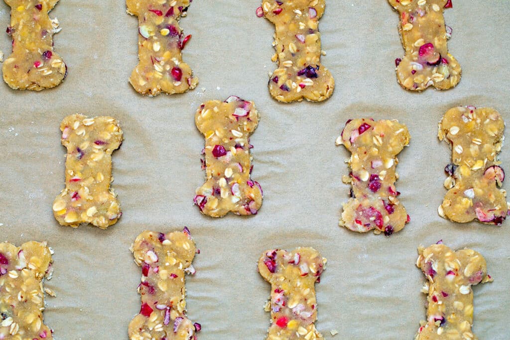 Cranberry dog treat cookie dough in bone shapes on cookie sheet.