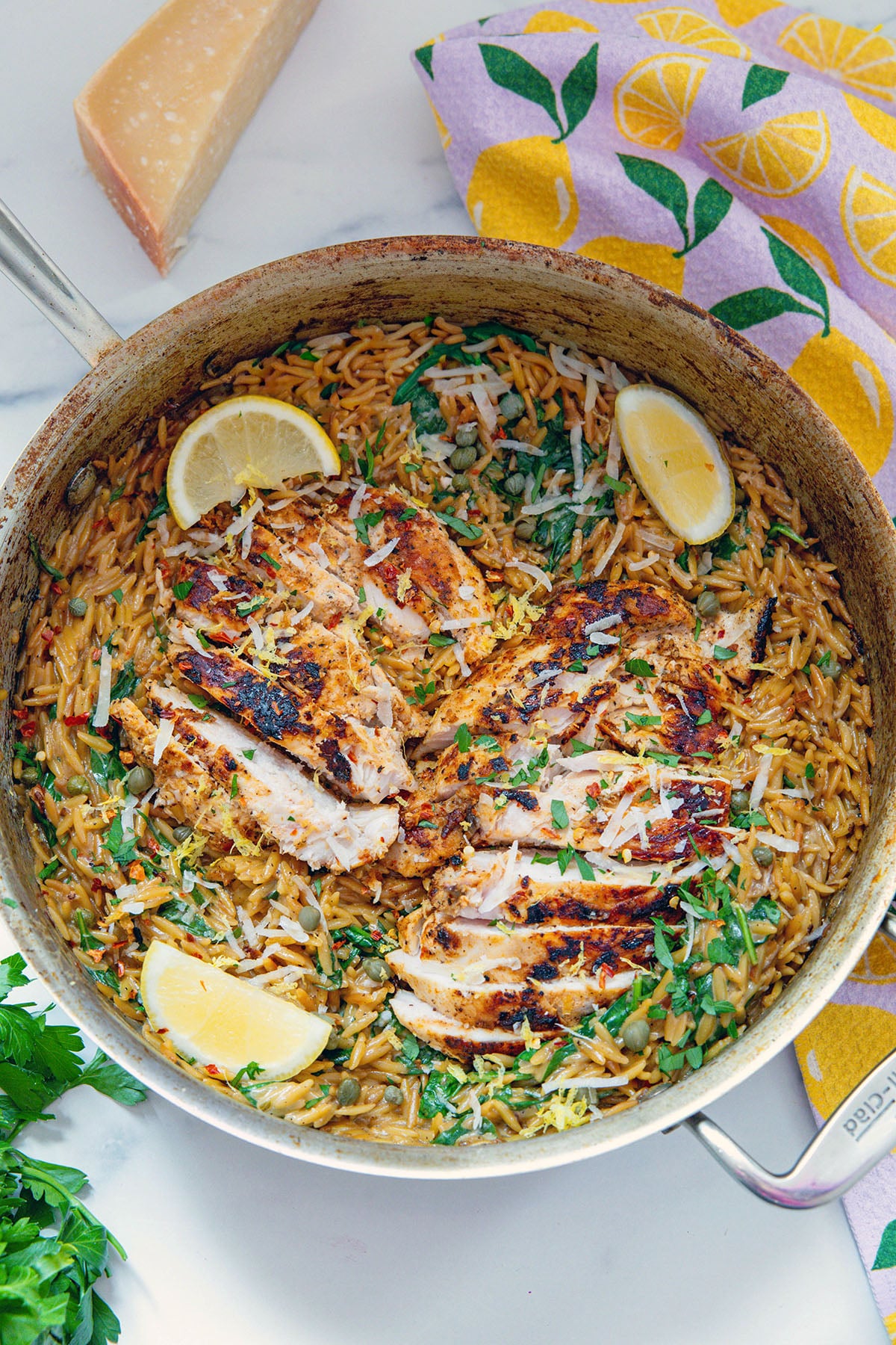Overhead view of creamy lemon orzo in a stainless steel skillet with sliced chicken over the top.