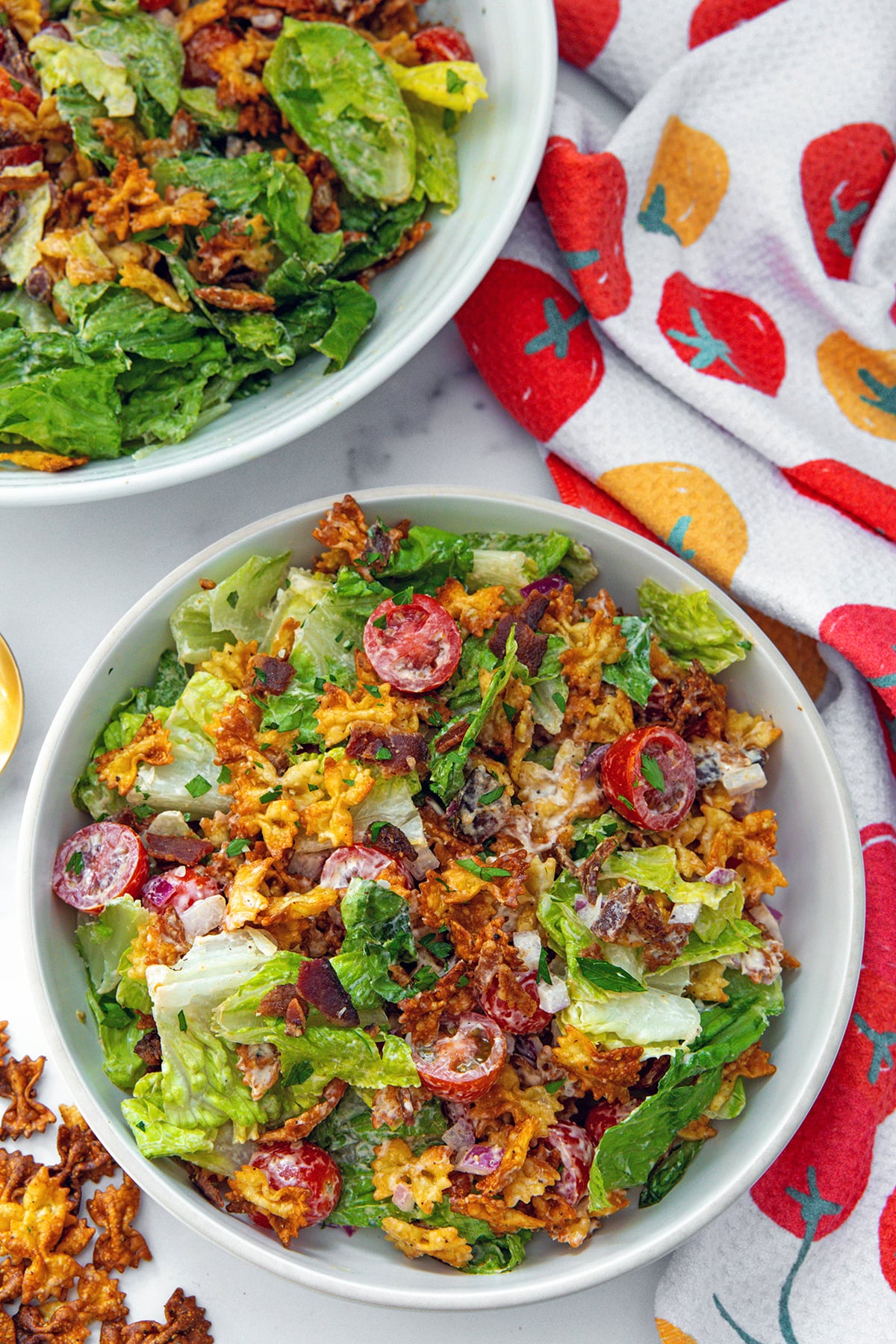 Bird's eye view of a bowl of crispy BLT pasta salad with second bowl in background and crispy pasta on the side.