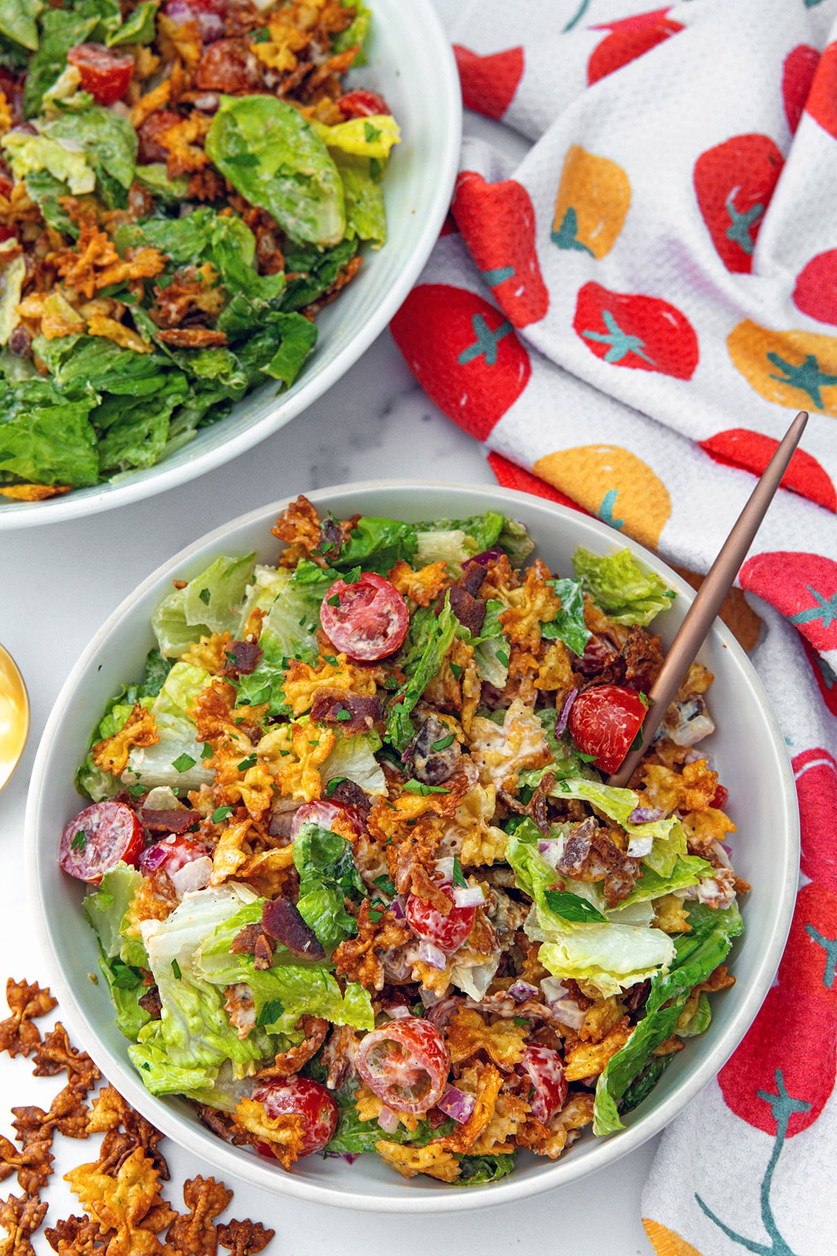 Overhead view of a a BLT salad with crispy pasta with second salad in the background, pasta on the side.