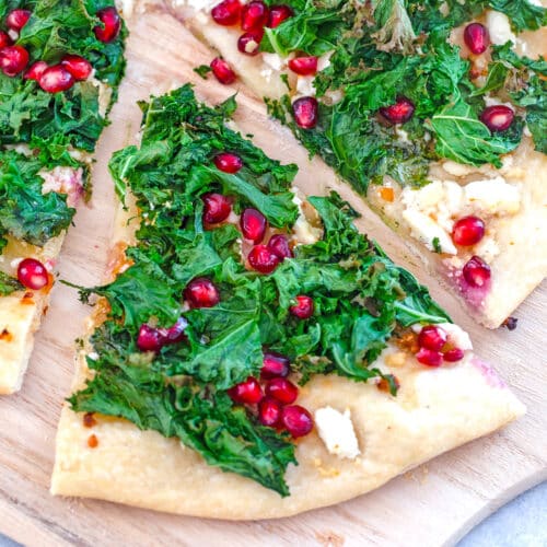 Closeup view of a slice of crispy kale and pomegranate flatbread pulled out from the rest of the pizza.