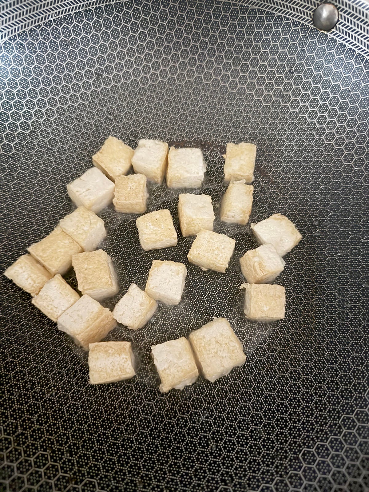 Cubed tofu caramelizing in wok.