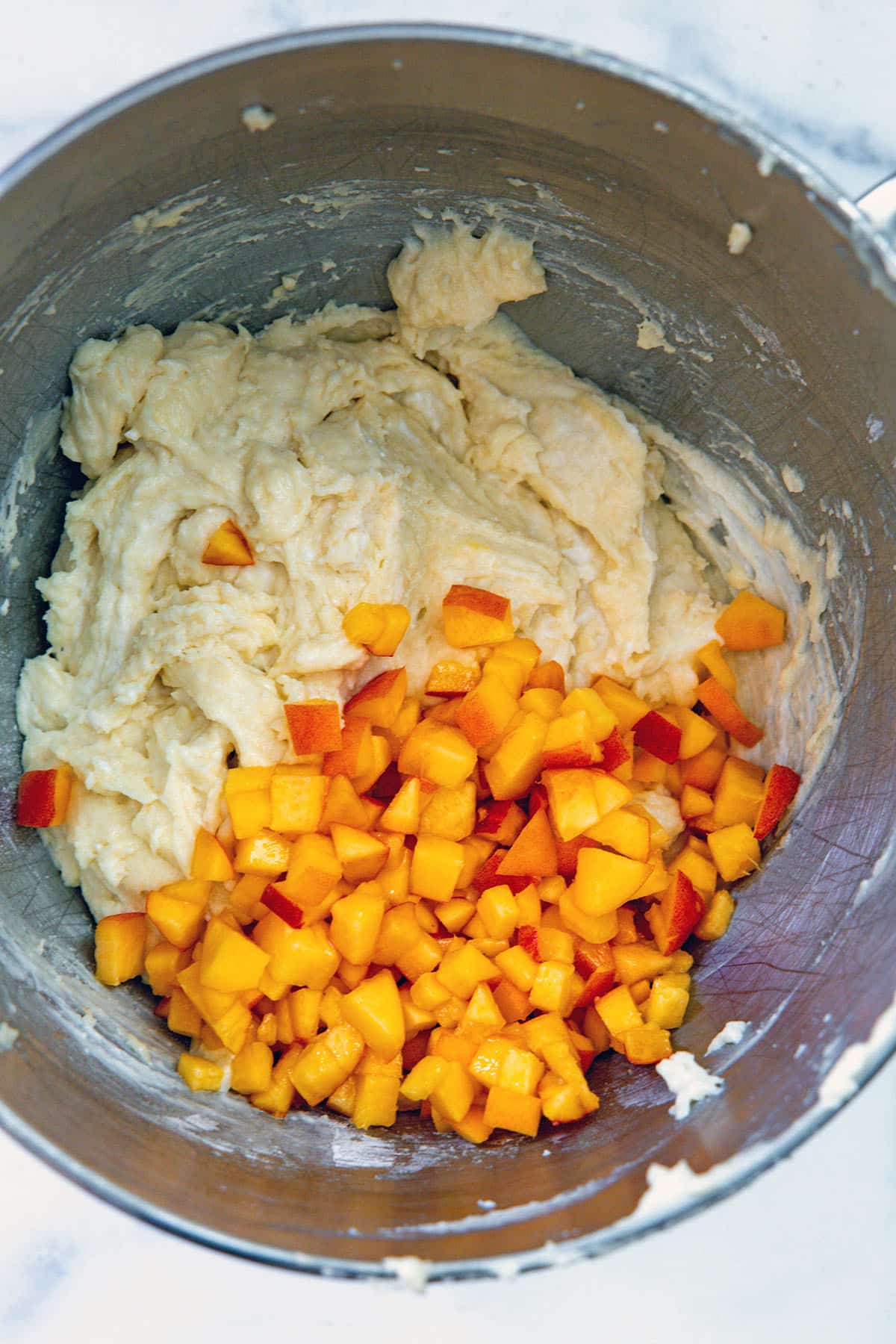 Cupcake batter in mixing bowl with diced peaches.