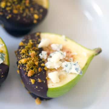 Closeup of a fig dipped in dark chocolate and pistachios with gorgonzola crumbled on top.