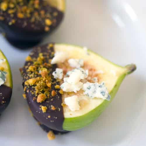 Closeup of a fig dipped in dark chocolate and pistachios with gorgonzola crumbled on top.