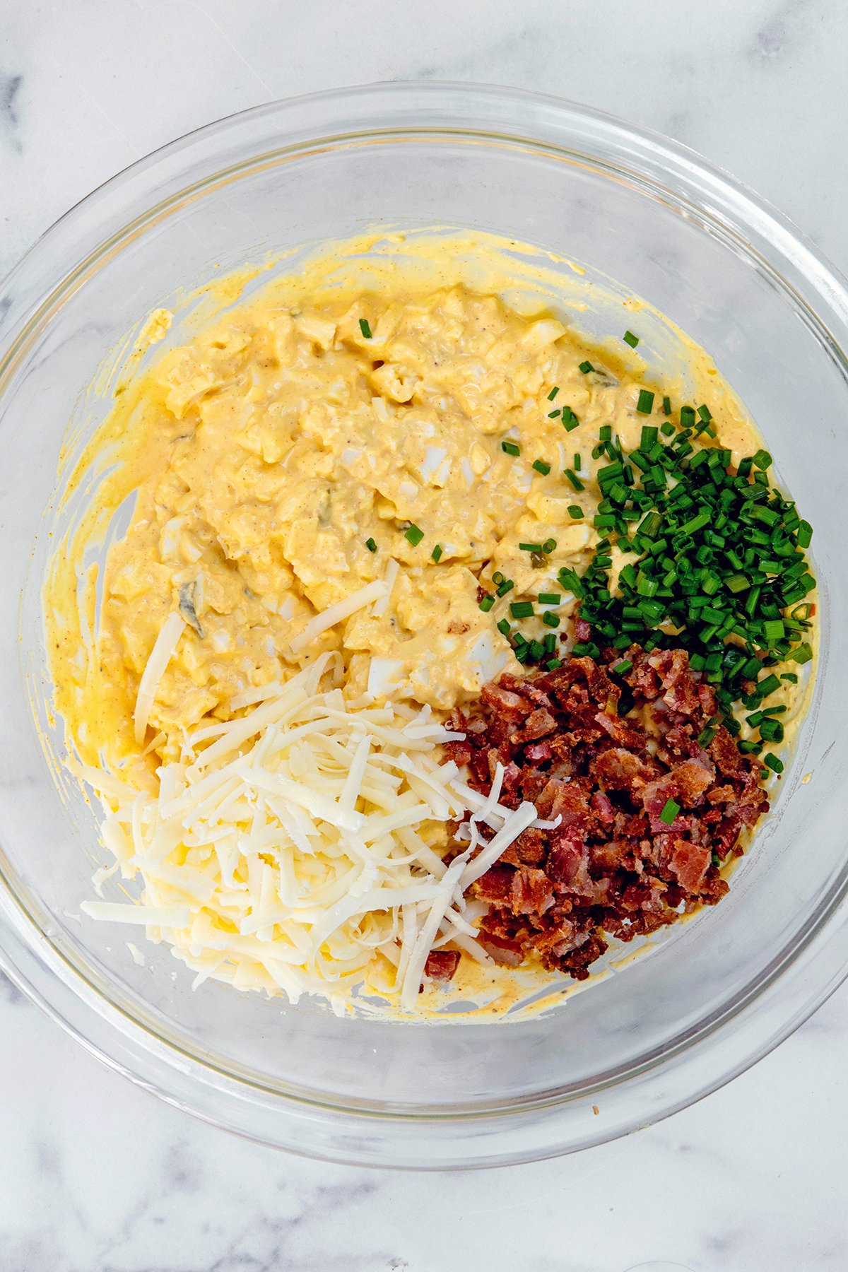 Deviled egg dip in bowl topped with chopped bacon, shredded cheese, and chives.