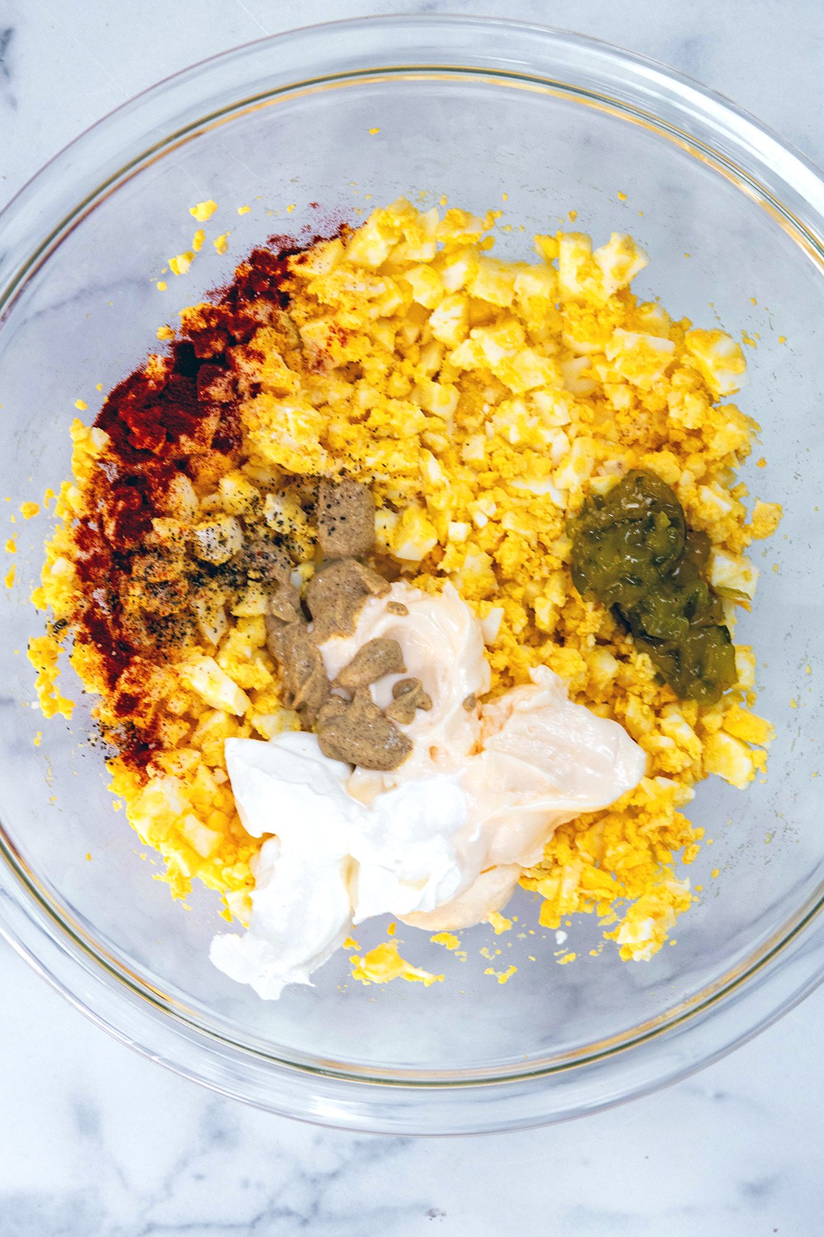 Hardboiled eggs mashed in bowl with mayo, mustard, relish, and seasonings.