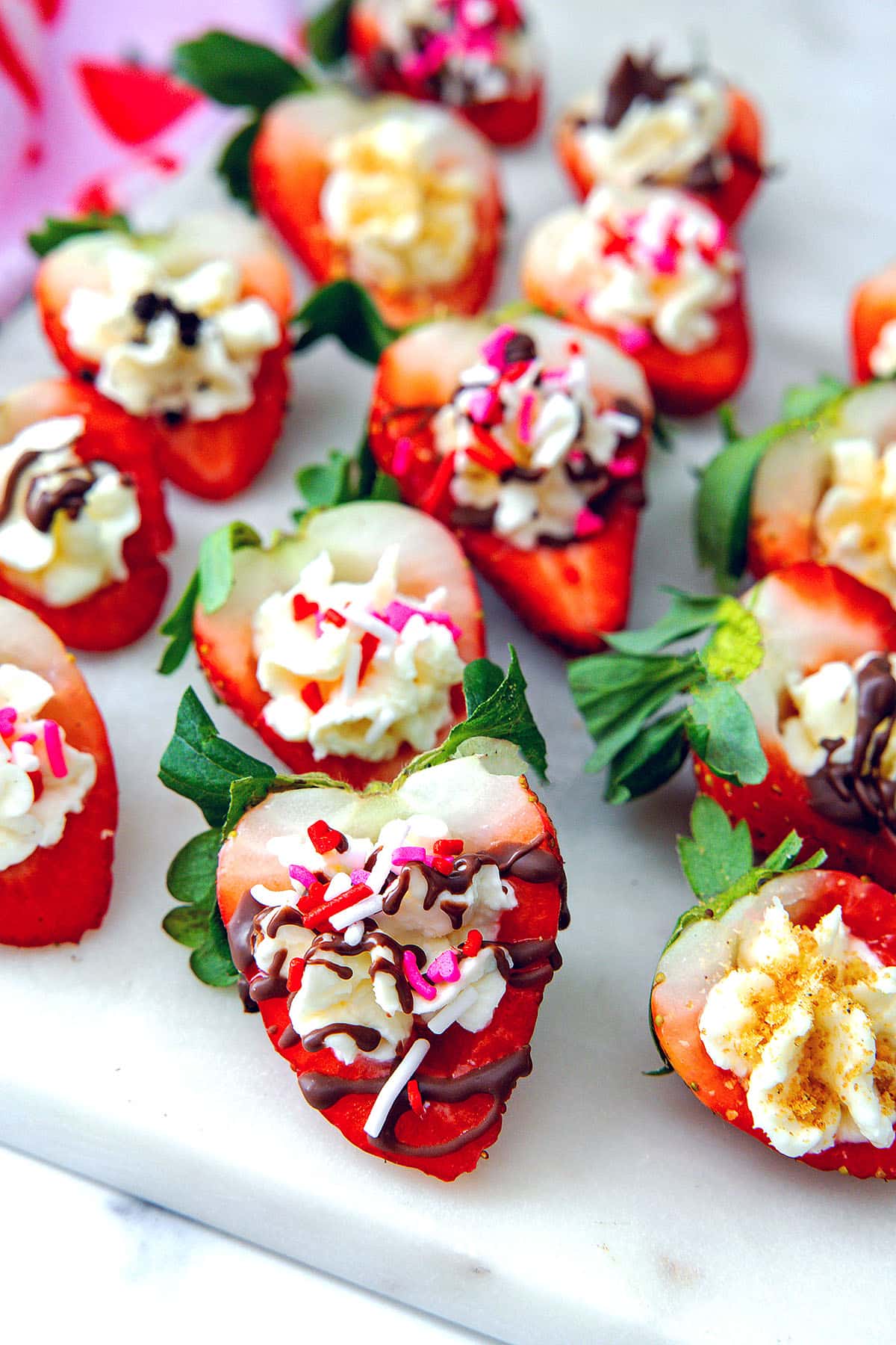 Strawberry halves filled with cream cheese filling and topped with chocolate drizzle, sprinkles, and graham cracker crumbs.