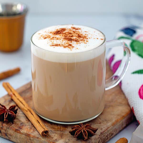 Closeup view of a dirty chai latte with cinnamon sticks and star anise all around.