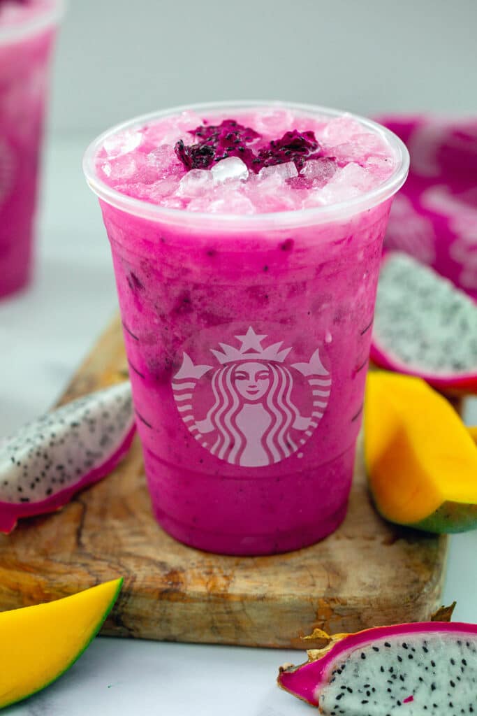 Bright magenta colored Dragon Drink in a Starbucks cup with sliced mango and dragon fruit all around.