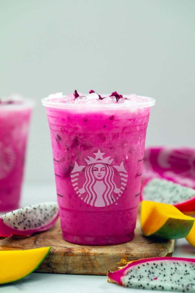 Head-on view of a Dragon Drink in a Starbucks cup with sliced mangoes and dragon fruit all around.