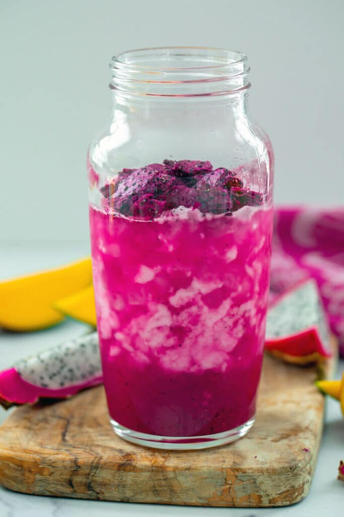 Mango Dragonfruit Refresher base mixed with coconut milk and freeze-dried dragon fruit pieces in a clear shaker.