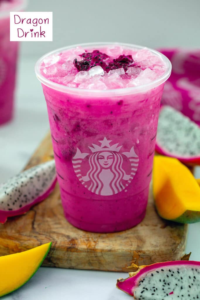 Bright magenta colored Dragon Drink in a Starbucks cup with sliced mango and dragon fruit all around and recipe title at top.