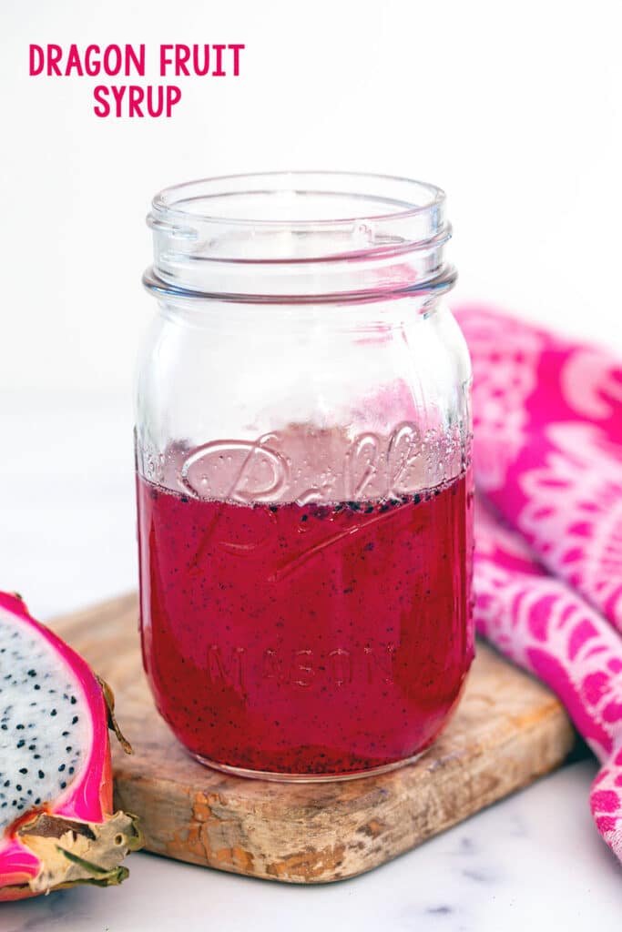 Head-on view of a mason jar of pink dragon fruit syrup with fresh dragonfruit half on the side and recipe title at top.