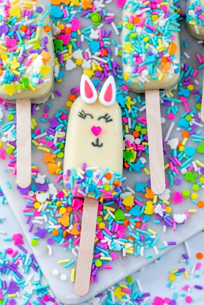 Overhead view of a bunny cakesicle with more cakesicles in background and sprinkles all around.