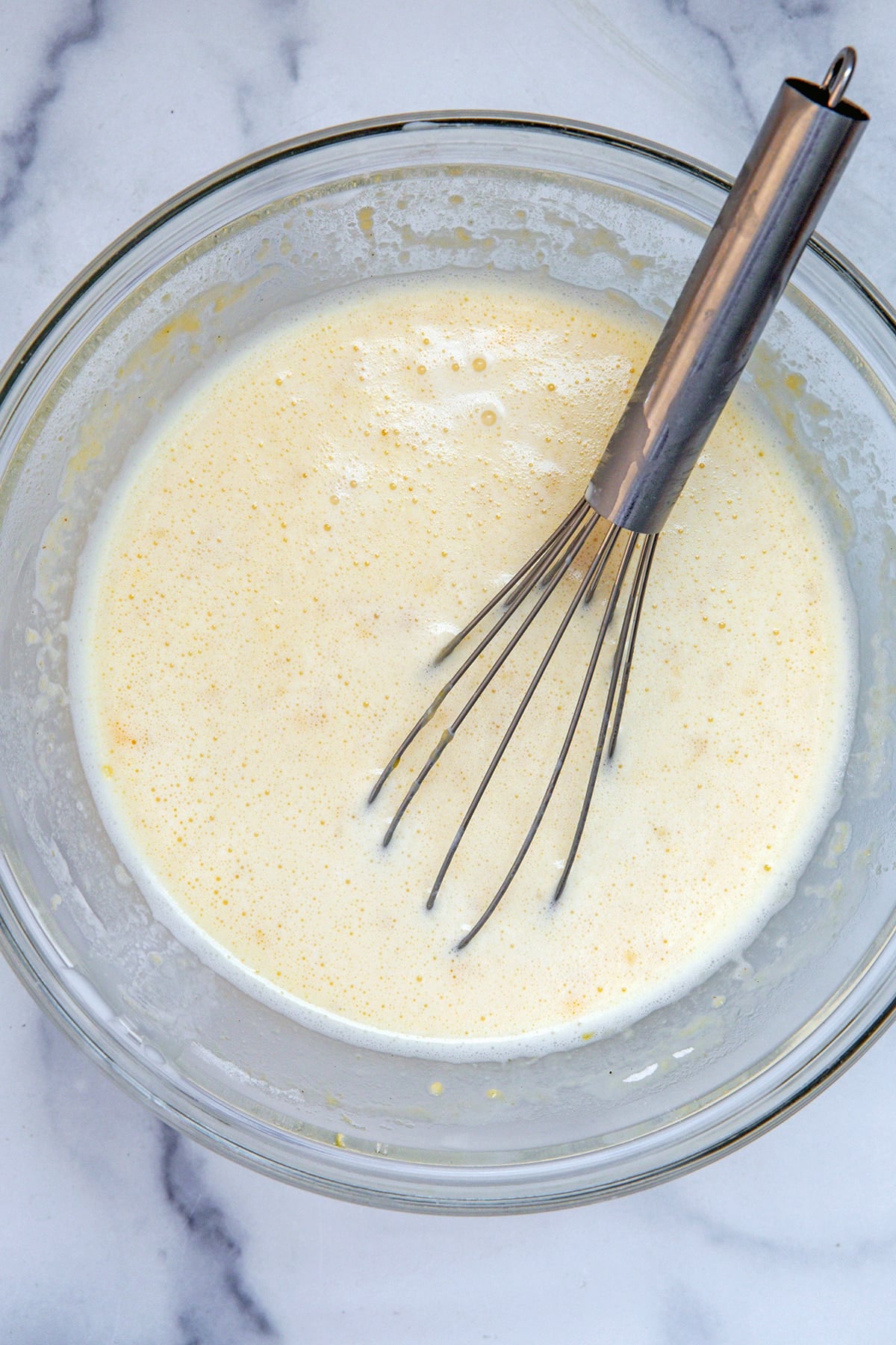 Eggs, heavy cream, milk, sugar, and spices in bowl with whisk.