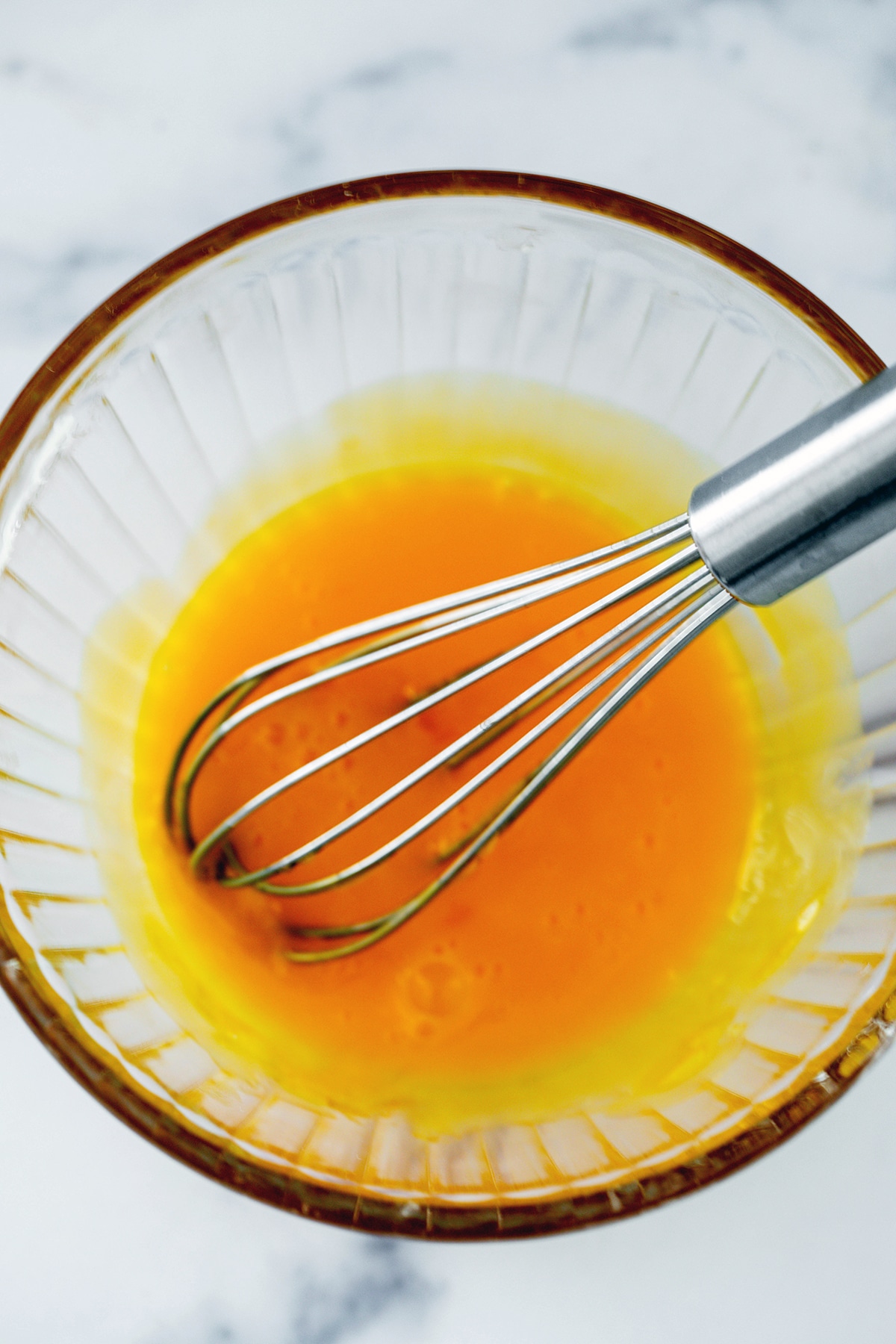 Egg yolks whisked together in bowl with whisk.