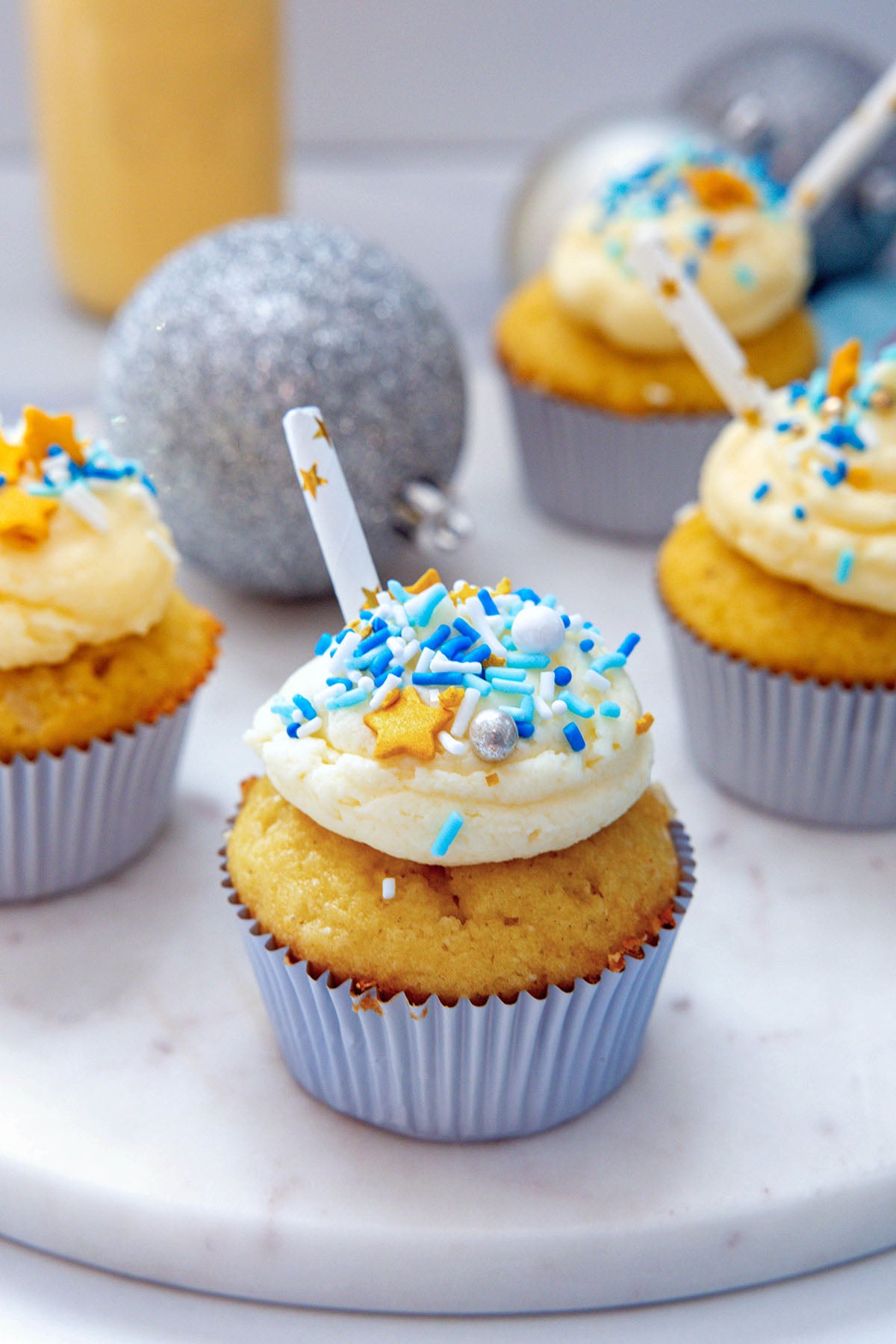 Eggnog cupcakes with buttercream frosting, blue sprinkles, and straws with silver ornament.