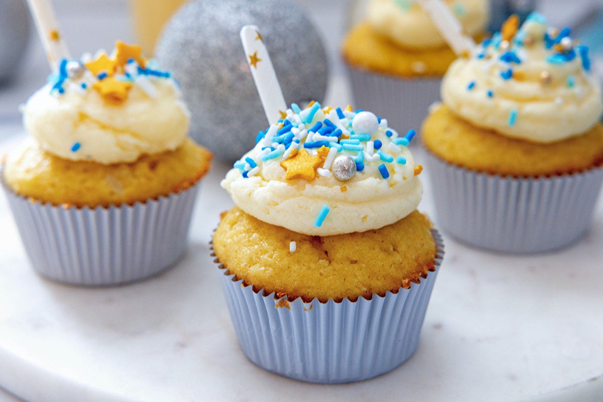 Landscape head-on view of eggnog cupcakes with buttercream and blue sprinkles on a marble surface.
