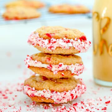 Closeup view of a stack of eggnog peppermint sandwich cookies with crushed candy cane all around.