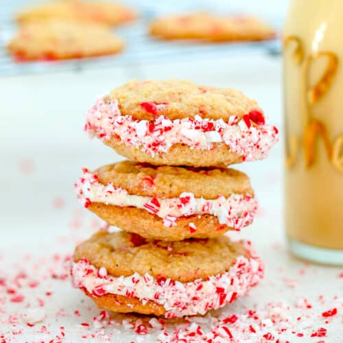 Closeup view of a stack of eggnog peppermint sandwich cookies with crushed candy cane all around.
