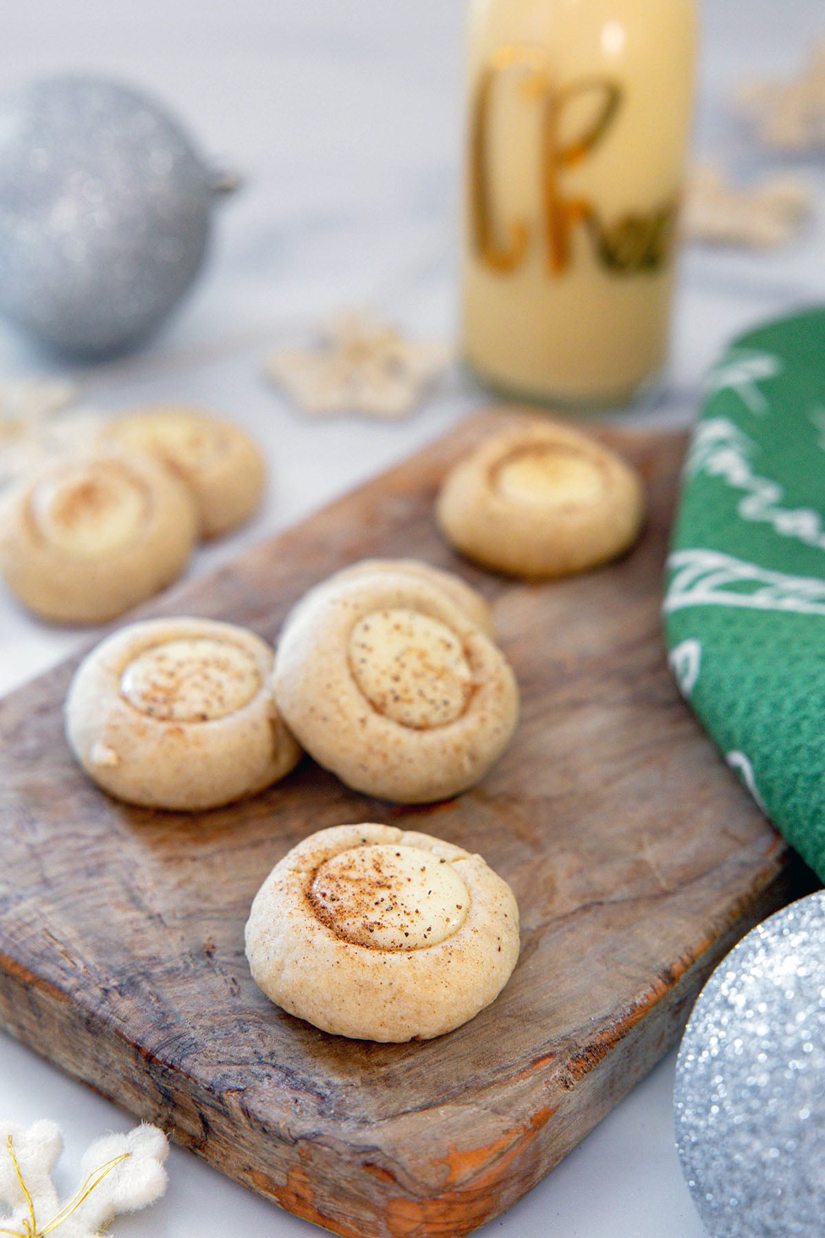 Eggnog thumbprint cookies filled with icing on a wooden board with bottle of eggnog in background.