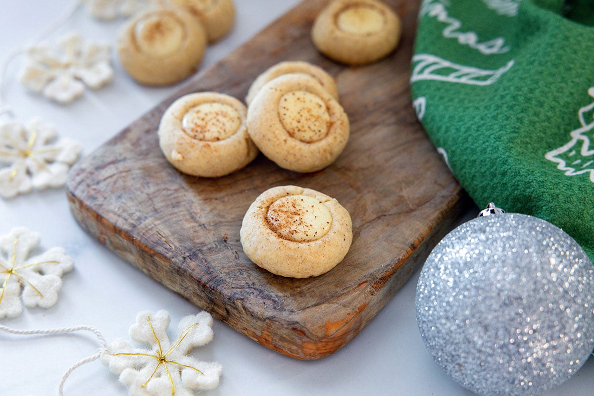 Landscape view of eggnog thumbprint cookies with snowflakes and silver ornaments all around.