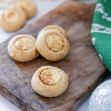 Closeup view of eggnog thumbprint cookies on a wooden board.