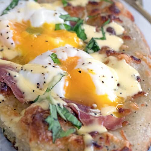 Closeup view of eggs benedict pizza with runny eggs and hollandaise on top.