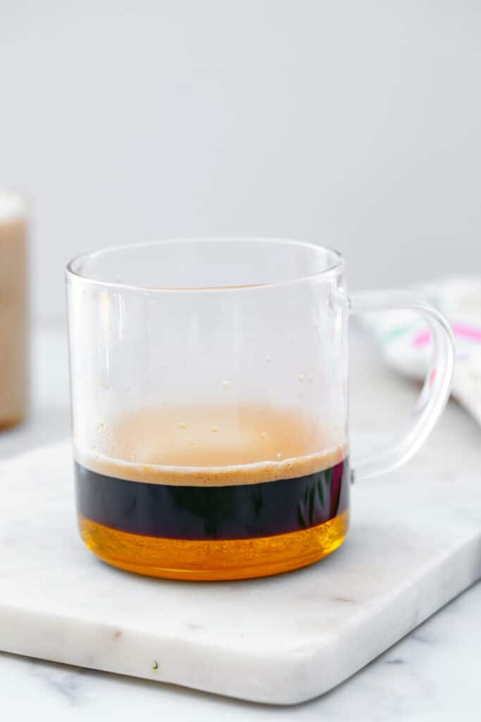 Caramel syrup and espresso at the bottom of a clear mug.