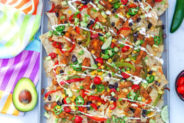 Landscape overhead view of chicken fajita nachos on a sheet pan with avocado half, jalapeño pepper, and tomatoes on the side.