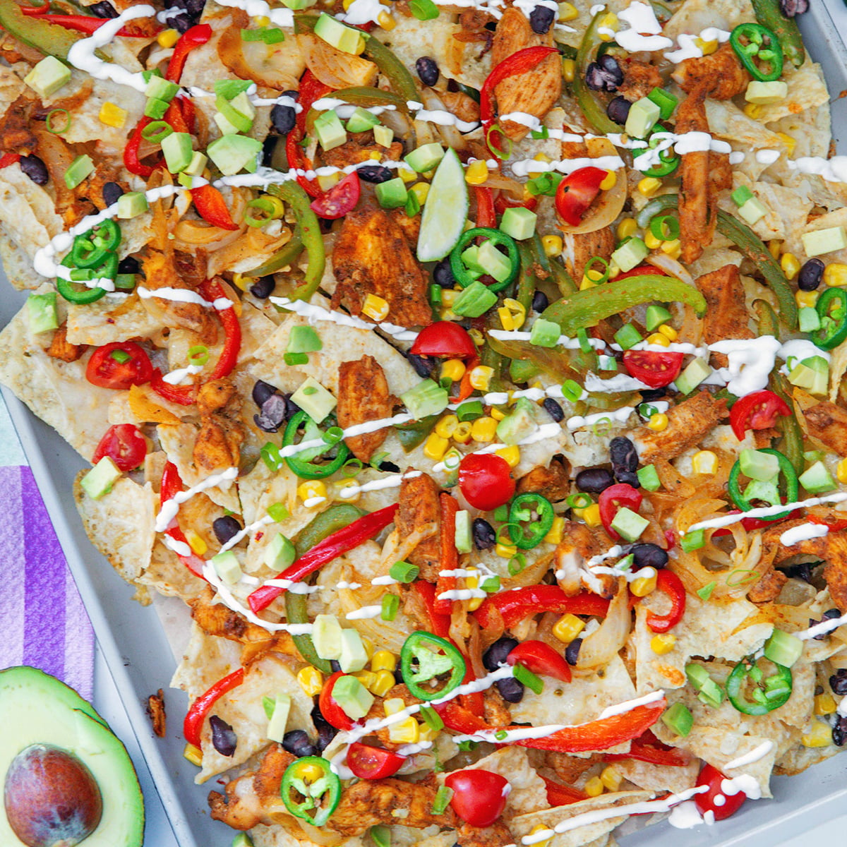 Closeup view of chicken fajita nachos with avocado, tomato, black beans, peppers, sour cream, and more.