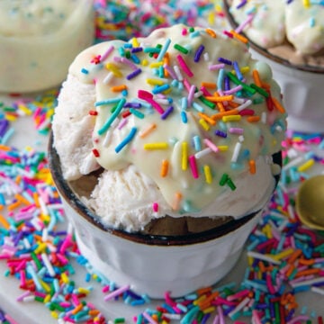 Closeup view of a scoop of ice cream in a bowl topped with white chocolate funfetti magic shell.