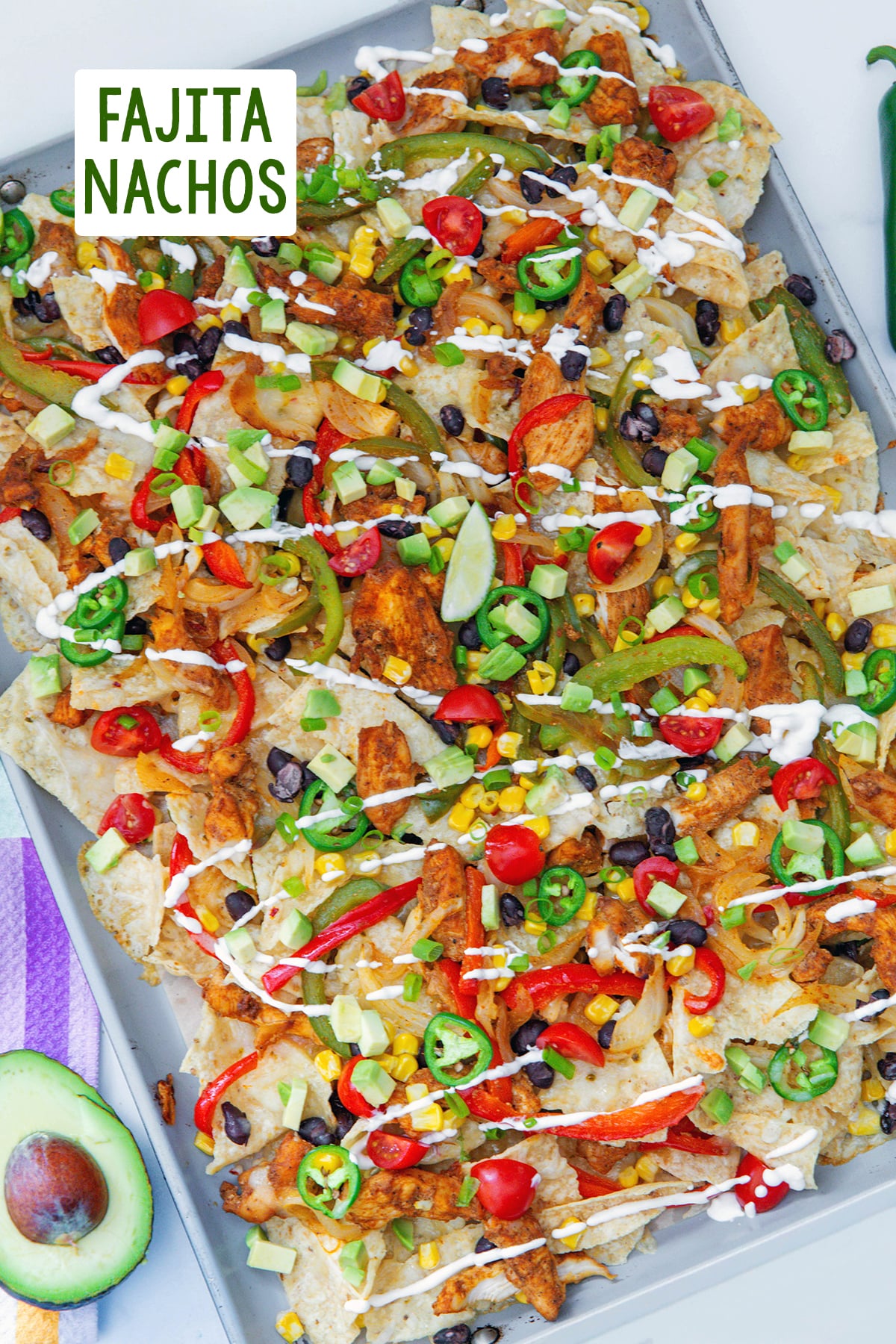 Overhead view of chicken fajita nachos on a sheet pan with avocado on the side and recipe title at top.