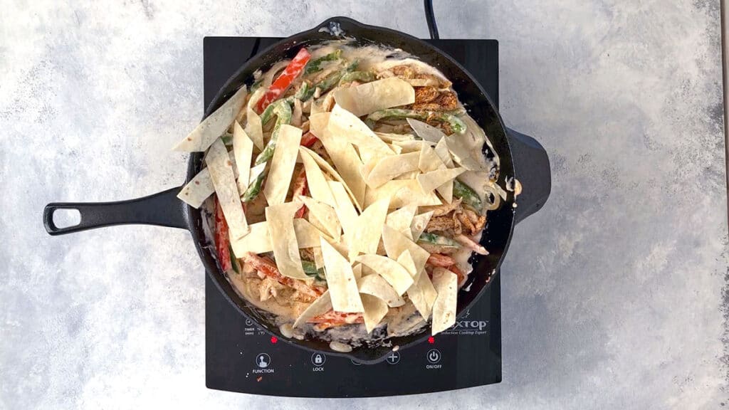 Tortilla strips topping skillet with chicken, peppers, and creamy sour cream sauce.