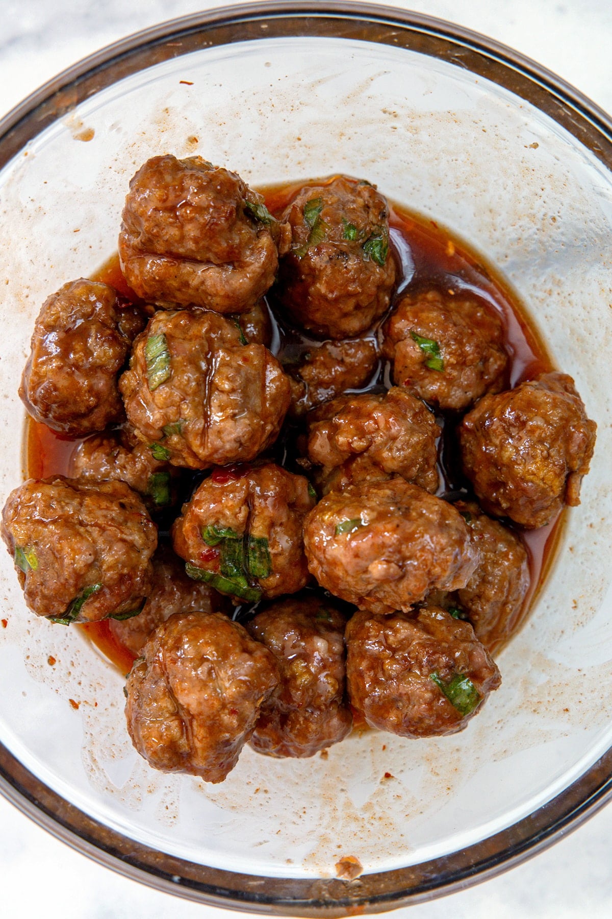 Meatballs in a bowl being tossed in spicy and sweet sauce.
