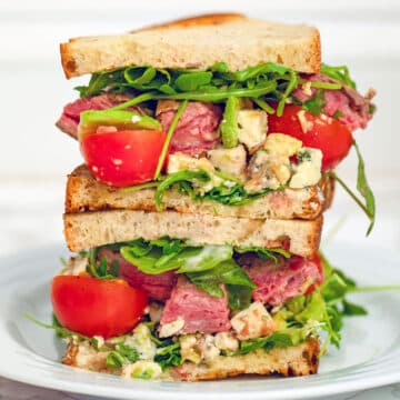 closeup view of a flank steak sandwich with arugula, tomato, and gorgonzola.