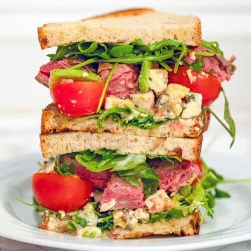 closeup view of a flank steak sandwich with arugula, tomato, and gorgonzola.