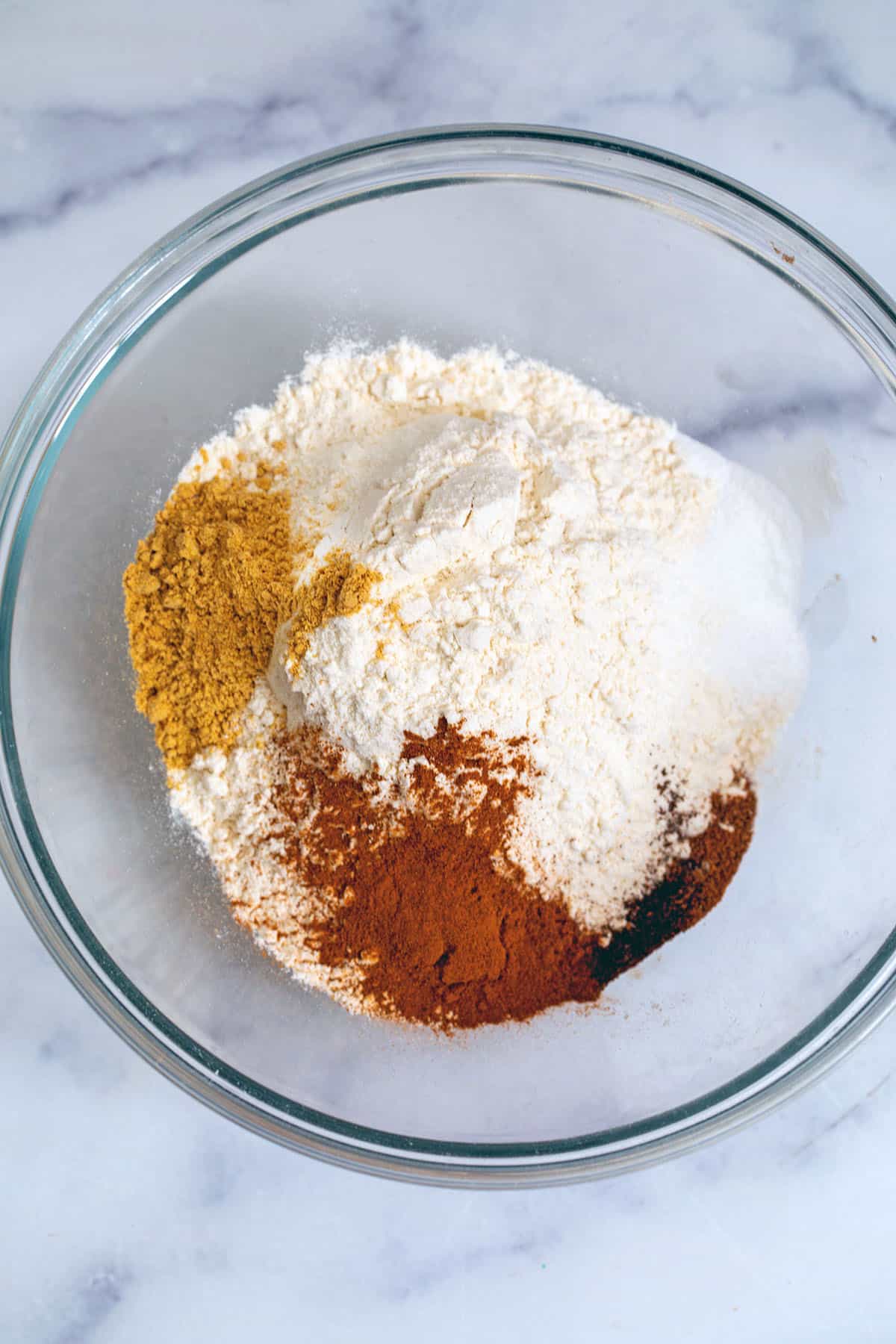 Flour in a bowl with ginger, cinnamon, cloves, and nutmeg.