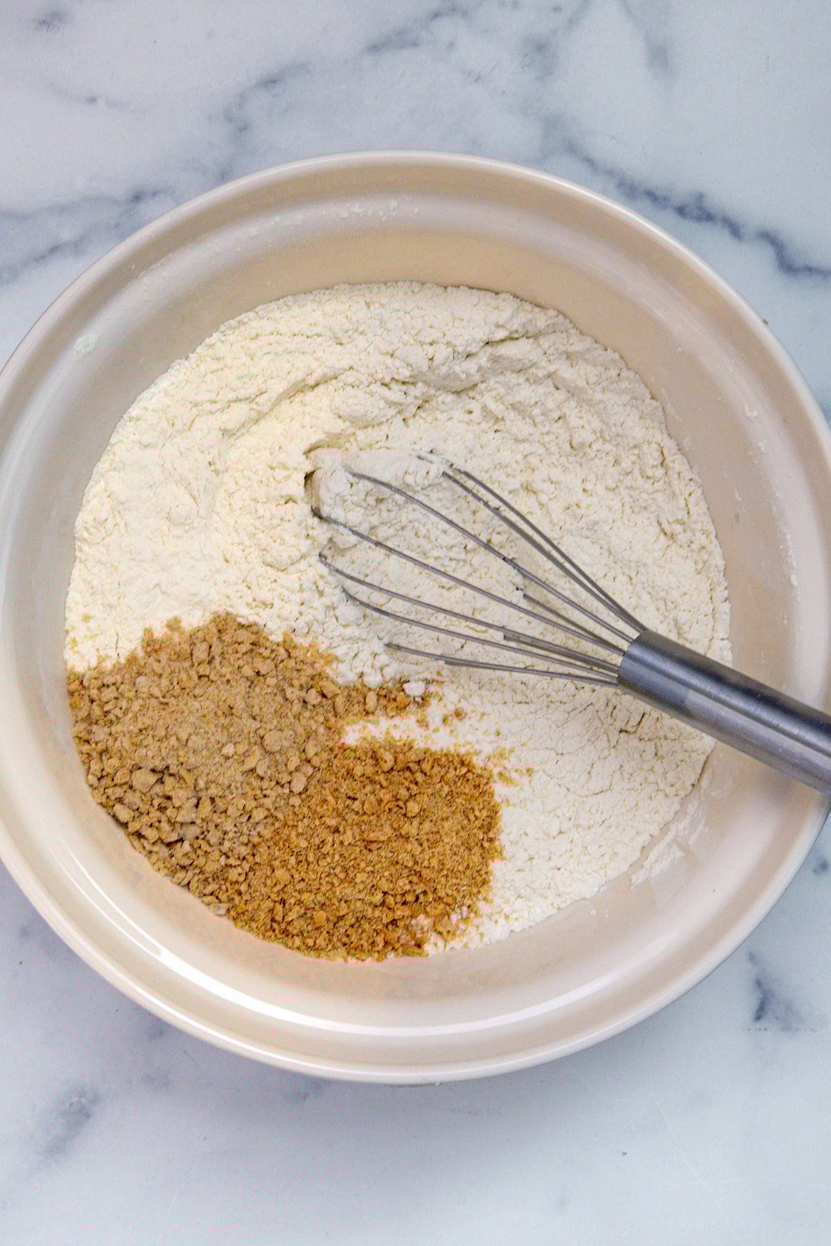 Overhead view of mixing bowl with flour, Lucky Charms oat cereal crumbs, and graham cracker crumbs.