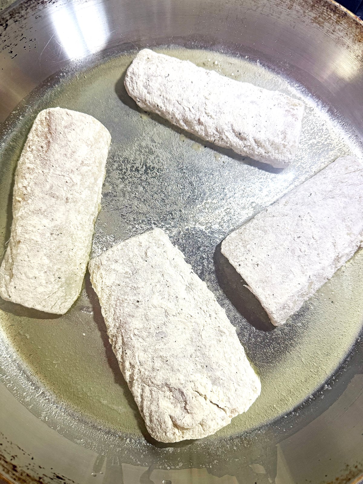 Floured cod filets in a skillet with butter and olive oil.
