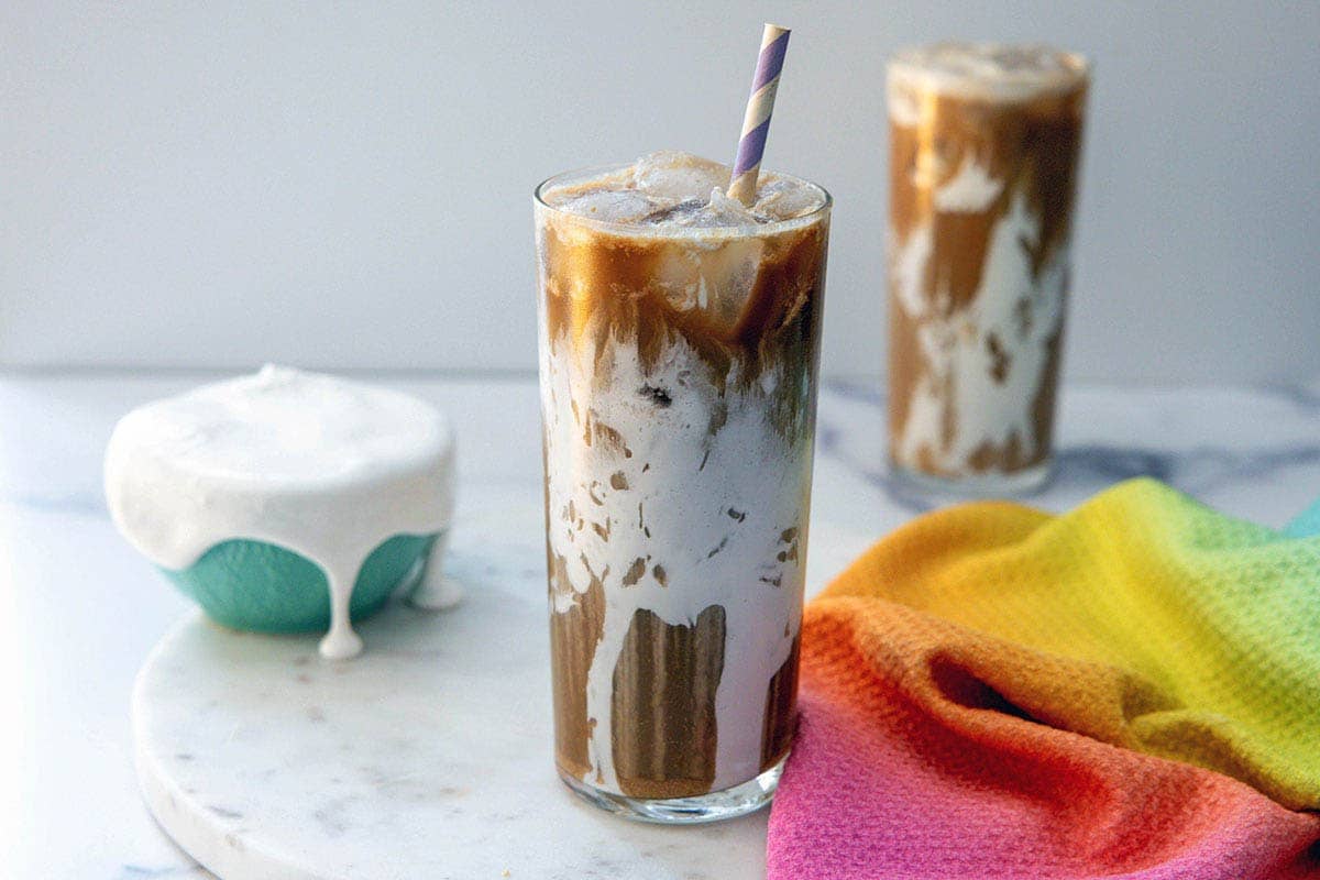 Landscape head-on view of a fluff seagull coffee drink with straw, second drink in background, and bowl of fluff.