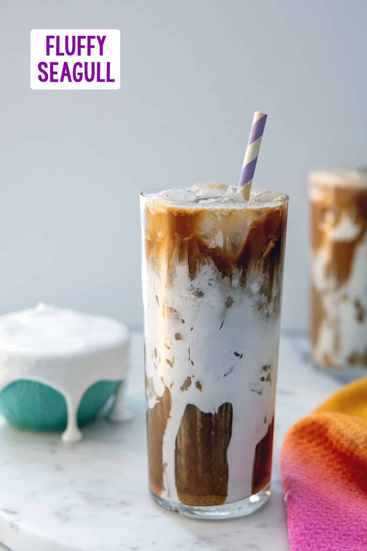 Head-on view of a Fluffy Seagull coffee drink in a fluff-lined glass with second drink and bowl of fluff in background and recipe title at top.