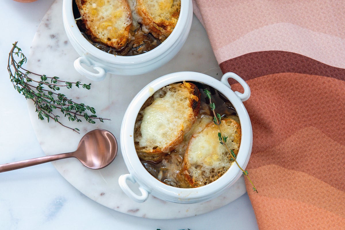 Landscape overhead view of two crocks of french onion chicken soup with bunch of thyme and spoon on the side.