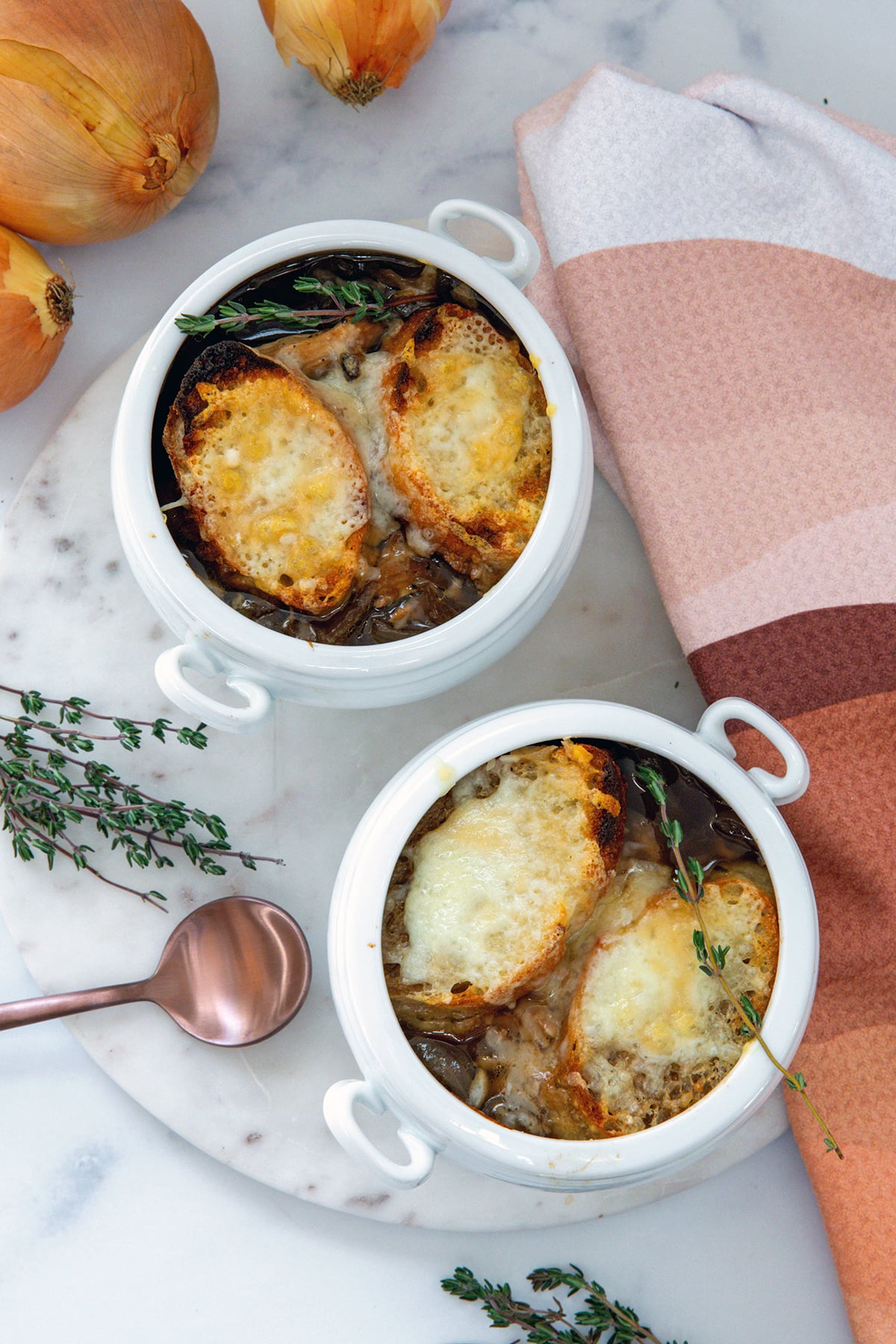 Overhead of two bowls of french onion chicken soup with bunches of thyme, onions, and a spoon.