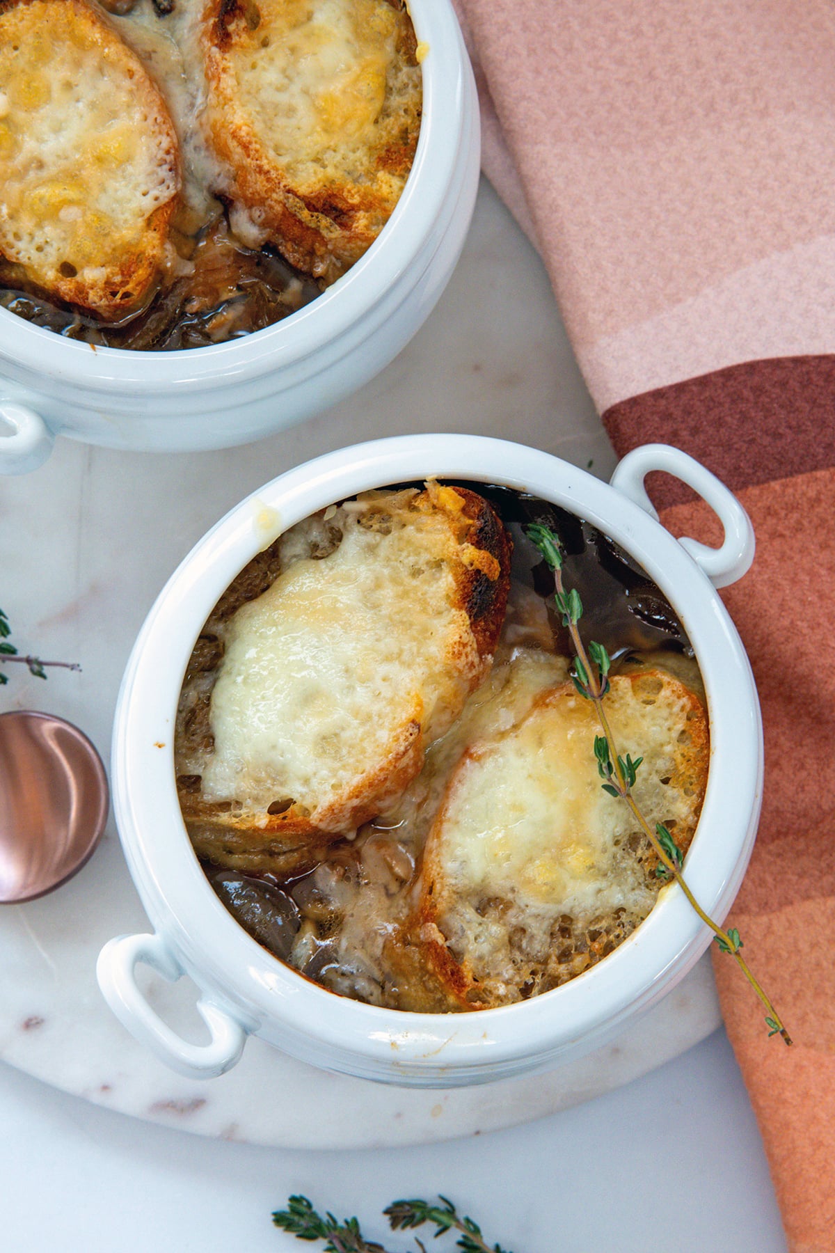 Overhead closeup view of a crock of french onion chicken soup with toasted bread, melted cheese, and thyme.