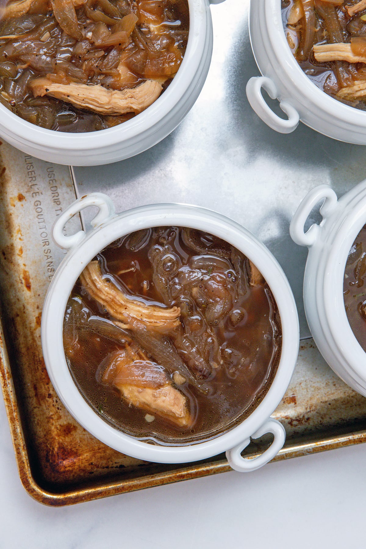 Overhead view of white crocks full of french onion chicken soup.