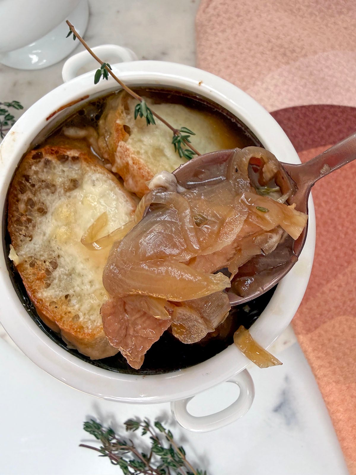 Spoon holding up french onion chicken soup over bowl.