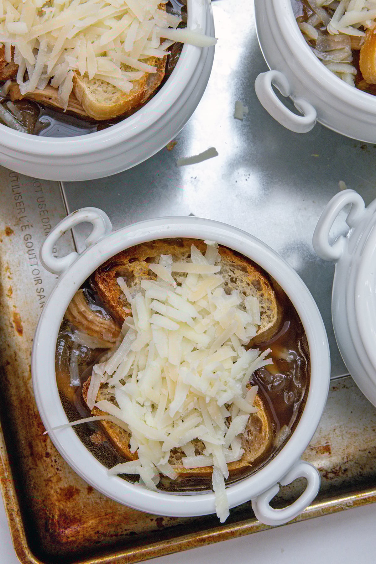 White crock of french onion chicken soup with tasted bread and shredded cheese on top.